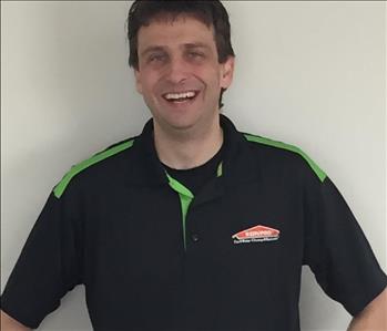 Man with dark hair smiling for employee photo with a black and green Servpro polo on. 