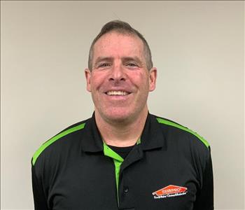 Man with short hair smiling for employee photo with black and green Servpro polo on. 