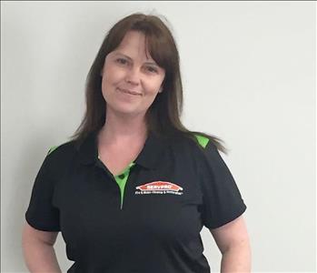 Woman with darker hair smiling for employee photo with black and green Servpro polo shirt on. 